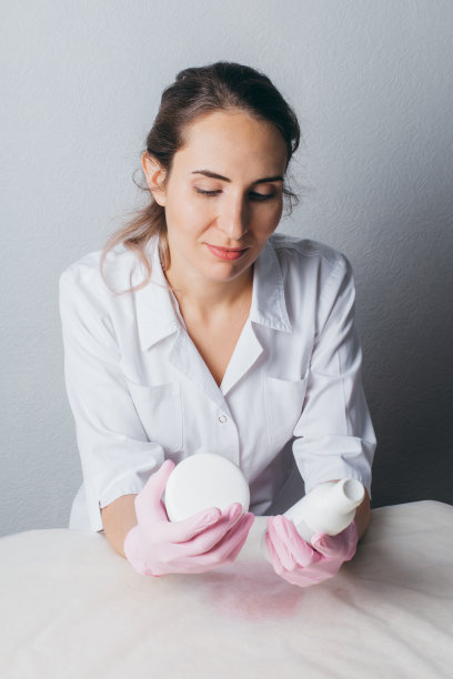 穿着白色制服，戴着粉色手套的美容师手里拿着一个装有化妆品的罐子和瓶子。图片下载