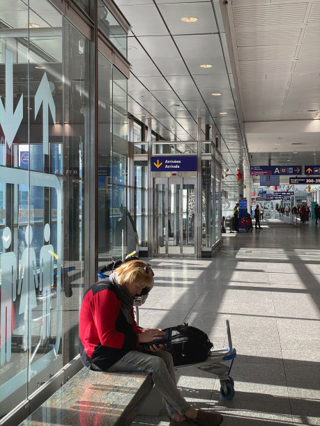 一位即将去度假的高级女士，在机场等待的时候正在用手机工作。图片下载