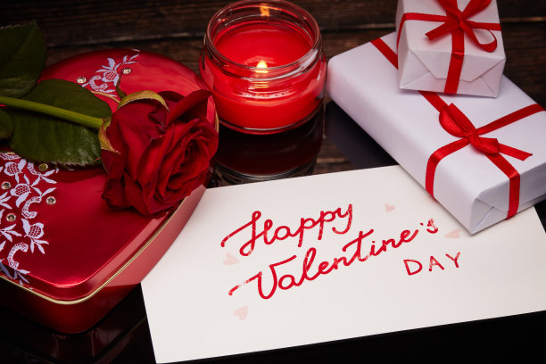 礼品盒，红玫瑰，燃烧的蜡烛和问候卡在深色的木制背景。情人节卡片图片下载