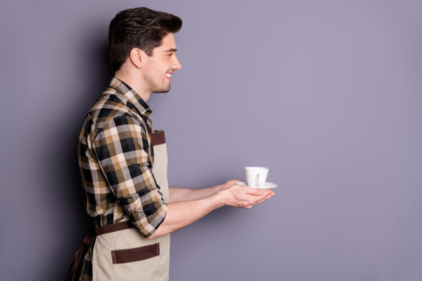 照片开朗积极英俊有吸引力的男人微笑，牙齿灿烂的服务杯茶给游客孤立的灰色背景图片下载