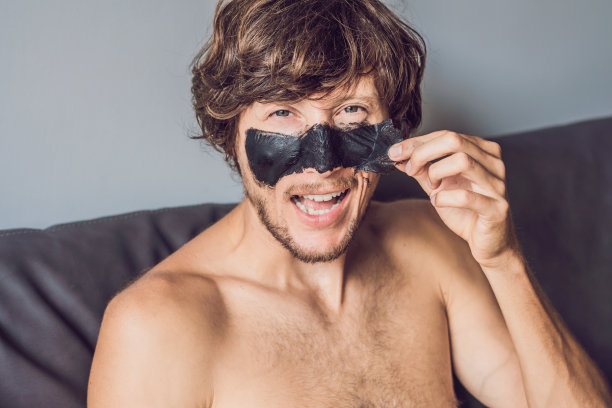 带着黑色面具的快乐男人。照片男子接受水疗。护肤理念图片下载