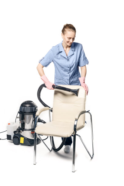 年轻的白人妇女穿着女保洁员制服正在用蒸汽清洗扶手椅，扶手椅孤立在白色的背景上。图片下载