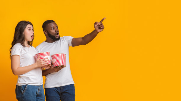 震惊的异族夫妇拿着爆米花，指着旁边的拷贝空间图片下载