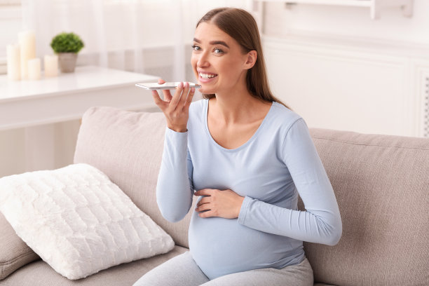 孕妇坐在家里沙发上使用智能手机扬声器图片下载