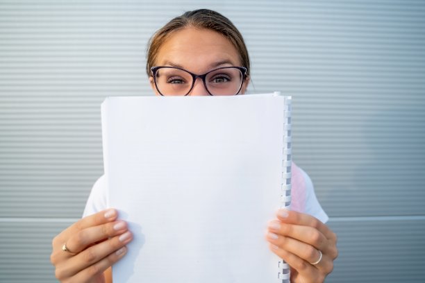 激动的女人与眉毛抬高掩盖她的脸的一半，举着空白便条本-库存照片图片下载