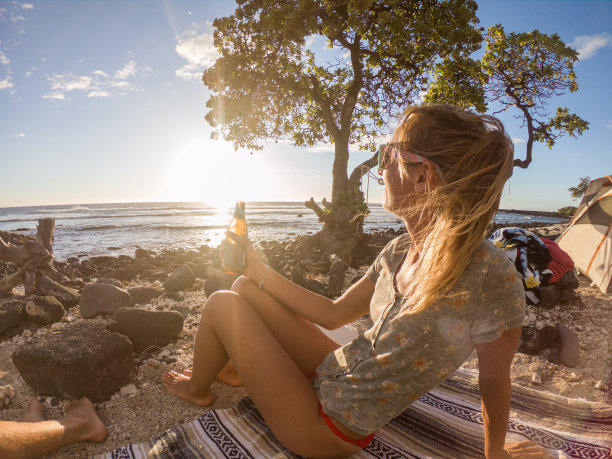 日落时分，年轻女子在海滩上喝酒图片下载
