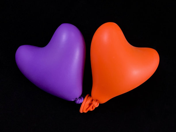在黑色的背景上，一个心形的明亮气球。两颗彩色的橡胶心。理念:两情相悦，形影不离，一统天下。图片下载