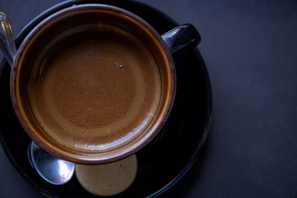 桌上的黑杯卡布奇诺咖啡，低调的照片。早上的咖啡杯和饼干。卡布奇诺特写，奶泡图片下载