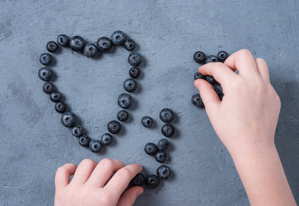 那孩子用手在蓝色的桌子上收集蓝莓。图片下载