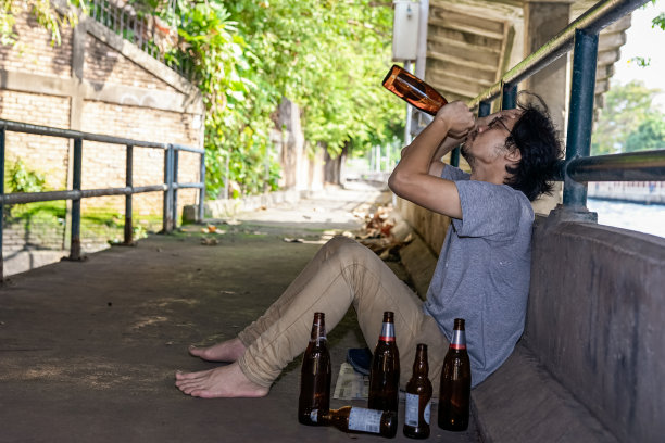 一个醉汉正在拿起一瓶酒喝。图片下载