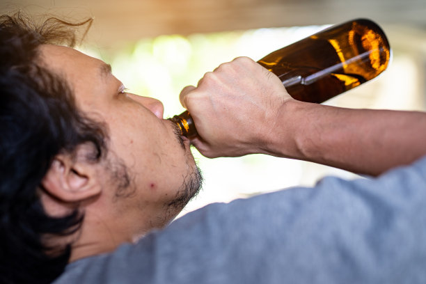 一个醉汉正在拿起一瓶酒喝。图片下载