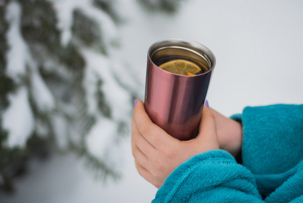 一个女孩手里拿着一杯柠檬热茶，背景是冬天的森林。冬天的概念。特写镜头,有选择性的重点图片下载