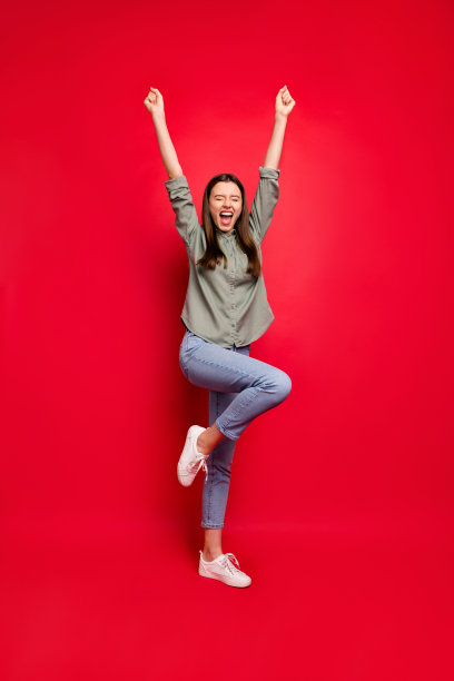 全身垂直的照片疯狂的女士举起拳头庆祝体育比赛胜利，欢呼尖叫穿休闲的灰色绿色衬衫牛仔裤孤立的红色背景图片下载