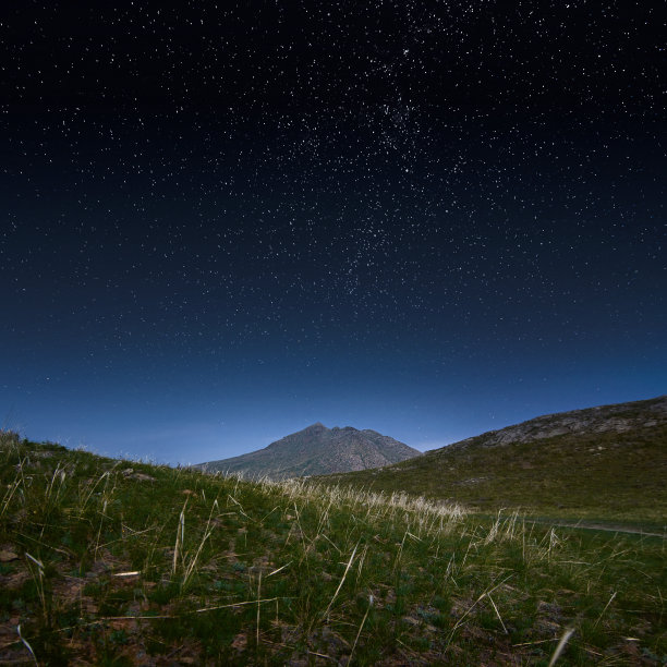 夜晚星空下的山丘和草原。素材图片