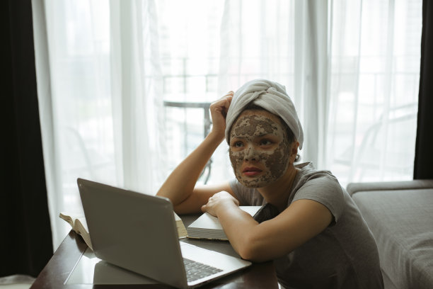 漂亮的女士在家里工作，而她的头发包裹着浴巾和面霜面膜图片下载