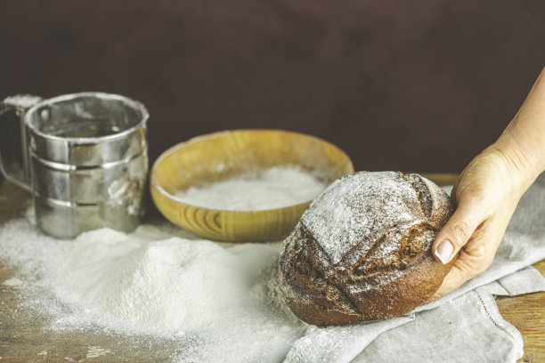 面包师的手拿着面包。高对比度照片。女人手里拿着黑麦面包，面包放在黑色的木桌上，上面撒着面粉图片下载