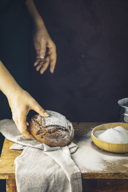 面包师的手拿着面包。高对比度照片。女人手里拿着黑麦面包，面包放在黑色的木桌上，上面撒着面粉图片下载