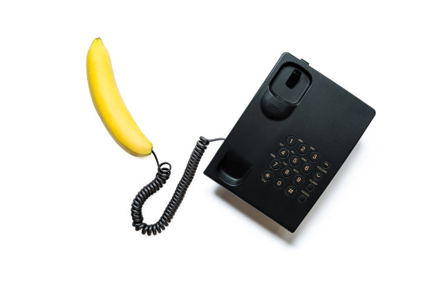 这是一个简单的现代黑色按键式电话，用亮黄色的香蕉代替了手机，孤立在白色的背景下。图片下载