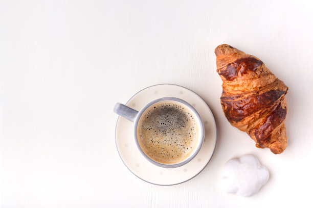 白木桌上放着羊角面包、上光的饼干和一杯咖啡。图片下载