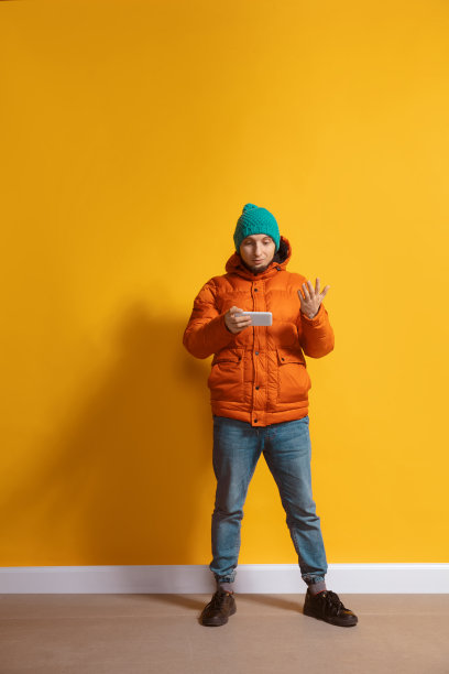 年轻的白人在用智能手机。全身长度肖像孤立在黄色背景。图片下载