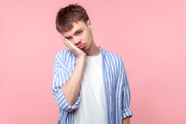 我很无聊。一个懒散的棕色头发的年轻男子的肖像，看起来疲倦和对相机不感兴趣。室内工作室拍摄孤立的粉红色背景图片下载