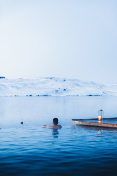 男人正在温泉池里洗澡，可以看到冰岛的雪山和冰湖图片下载