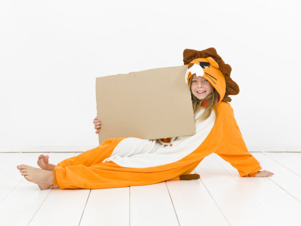 漂亮的金发女孩穿着舒适的狮子服装，在白色的墙壁前举着一个棕色的标志图片下载