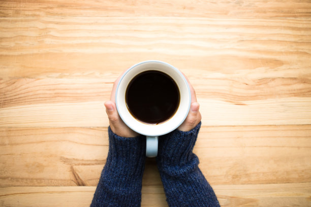 一个穿着蓝色毛衣的女人拿着一个咖啡杯放在一张旧木桌上。图片下载