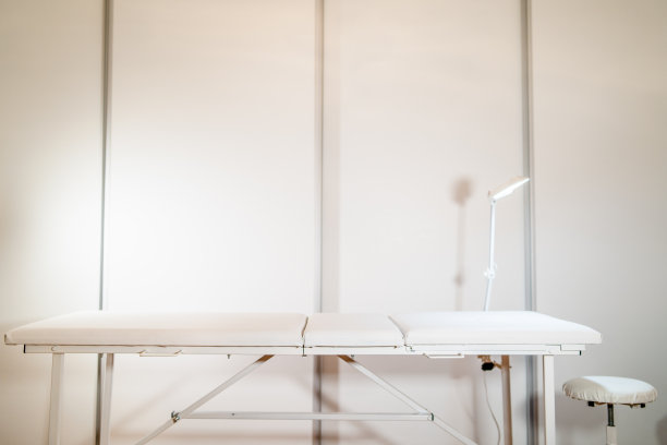 白色皮革按摩治疗桌前面的白色墙壁与灯在沙龙或水疗中心图片下载