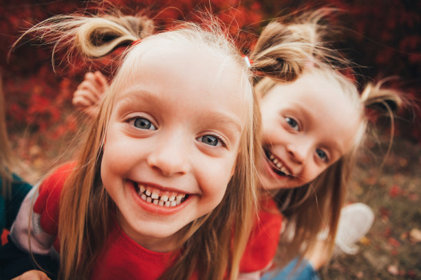 一对金发碧眼的双胞胎在红色树林的秋天森林里散步和玩耍。图片下载