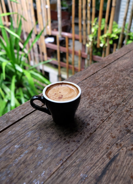热咖啡杯放在木桌上，以花园为自然背景，清晨雨天的种植园背景——意象图片下载