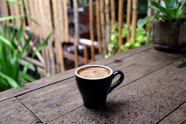 热咖啡杯放在木桌上，以花园为自然背景，清晨雨天的种植园背景——意象图片下载