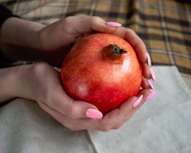 女孩的手拿着一个成熟的石榴对背景的格子图片下载