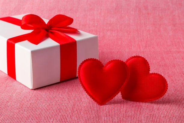 白色礼盒与红色丝带蝴蝶结和两个丝绸情人节的心在一个浅红色的纺织品背景。问候情人节卡片。爱的概念。图片下载