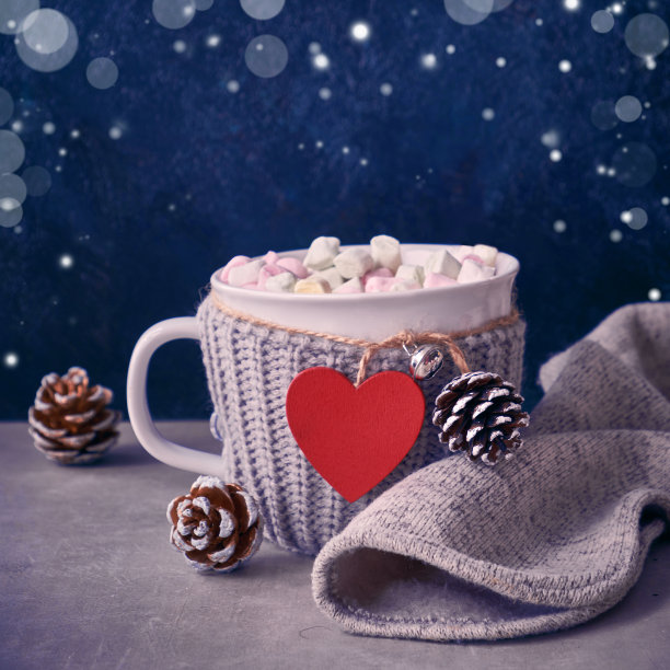 带棉花糖的热巧克力，桌上的杯子上有红心。带棉花糖的热巧克力，桌上的红心杯还有松果。冬季，非正式的生日或情人节背景图片下载