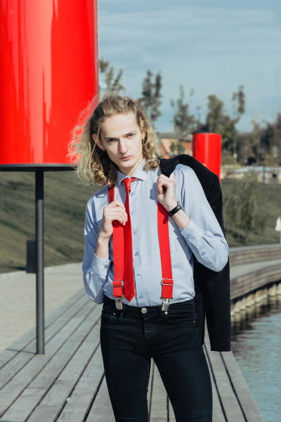 一名年轻英俊的男性模特的全长肖像穿着西装和红色领带和背带摆姿势在河堤上。图片下载