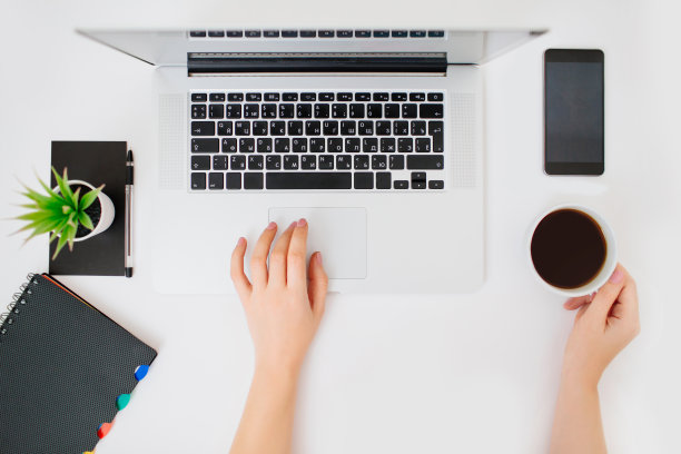 用手在笔记本电脑的键盘上打字。白色的桌子上。图片下载