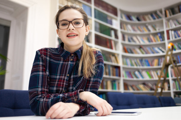 一位戴眼镜的年轻女学生坐在公共图书馆里图片下载