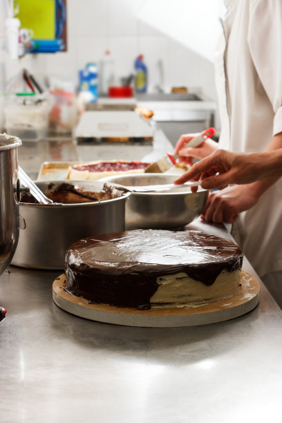 女士在巧克力蛋糕上涂上糖霜，这是烹饪的最后阶段。制作巧克力蛋糕的过程，从头到尾。手工制作的糖果。图片下载