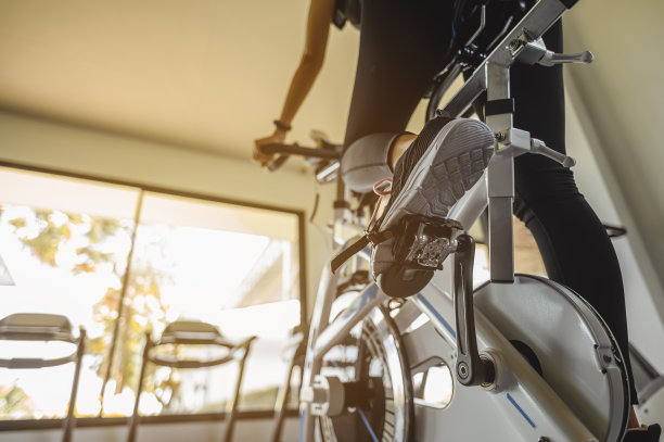 健身、健身、健身、生活方式和健康理念。后视图的女人锻炼与自行车。女性在日落时分在健身房里骑自行车进行健康的生活方式锻炼。图片下载