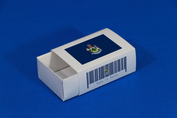 缅因州国旗上的白色盒子与条形码和颜色的州旗上的蓝色背景，纸包装放火柴或产品。出口贸易的概念。图片下载