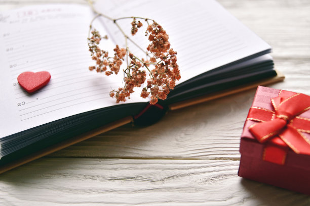 书摊上放着干花，白色木制背景上放着礼品盒。情人节的背景。图片下载
