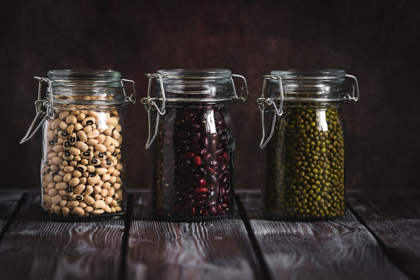 红色、绿色和白色的豆子装在罐子里，放在一张黑色的木桌上。素食和素食食品。图片下载