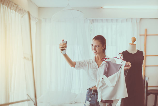 年轻美丽的女人站在服装店和选择衣服，快乐和微笑，时尚和生活理念图片下载