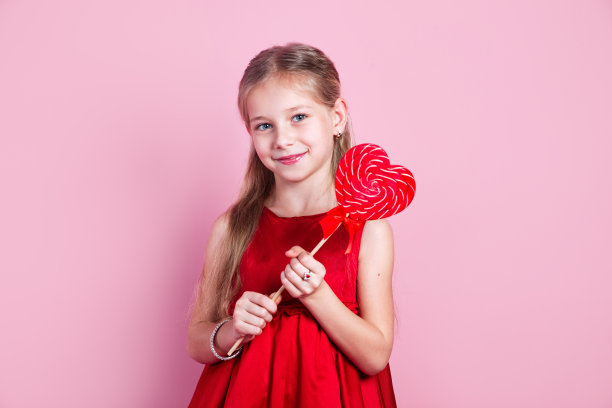 快乐的小女孩穿着红裙子，拿着心形棒棒糖图片下载