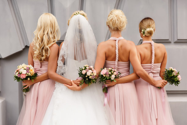 新娘和伴娘在婚礼当天穿着粉红色的礼服，手持花束摆姿势。快乐的婚姻和婚礼派对的概念图片下载