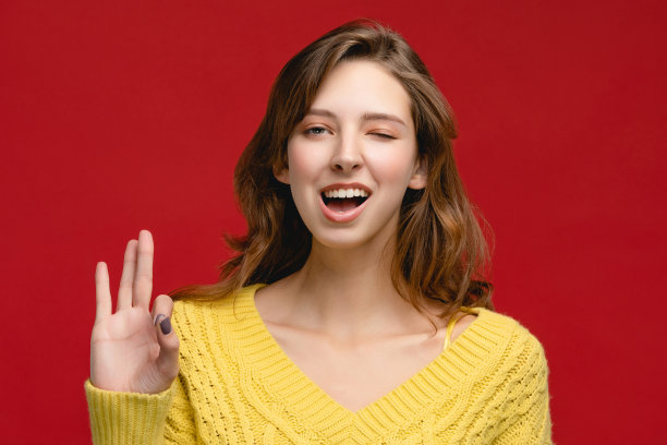 红色背景的演播室里，穿着黄色套头衫的开朗的白人年轻女性。图片下载