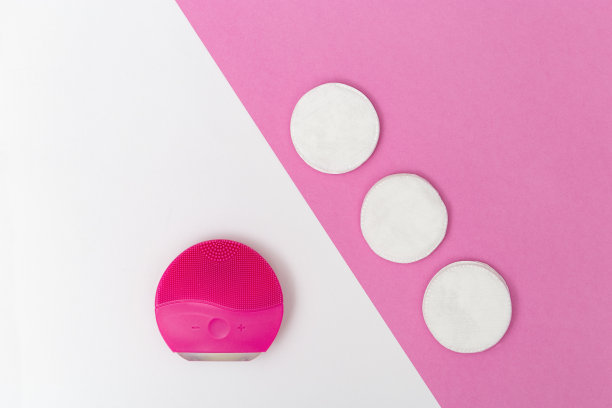 女性美容卫生用品，红色电动脸刷和棉垫在白色和粉红色的纸背景。面部护理。平的风格。前视图。图片下载