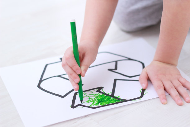 小男孩用绿色毡尖笔在育儿室的地板上画了一个回收标志。图片下载