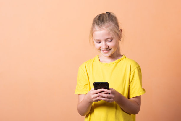 小女孩拿着智能手机，背景是浅橙色。图片下载